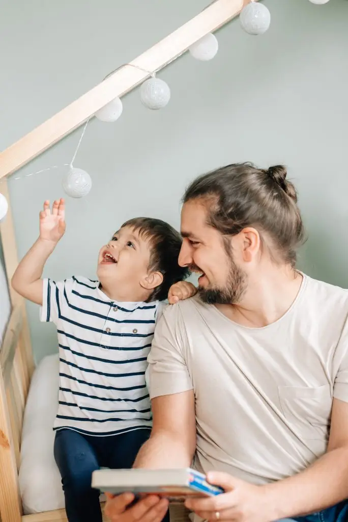 Spielerische Momente: Vater und Sohn genießen gemeinsam fröhliche Momente, während sie in der Newborn-Fotografie voller Freude miteinander spielen.